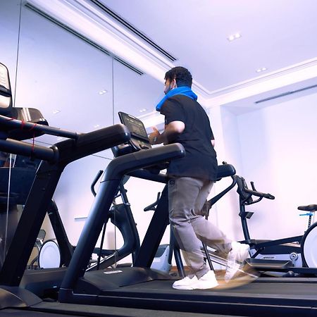 Makarem Ajyad Makkah Hotel Mekka Zewnętrze zdjęcie The photo shows a person exercising on a treadmill in a modern gym or fitness room. The individual is wearing a blue neck support while jogging on the treadmill, which is set against a backdrop of large mirrors. There are also additional exercise equ