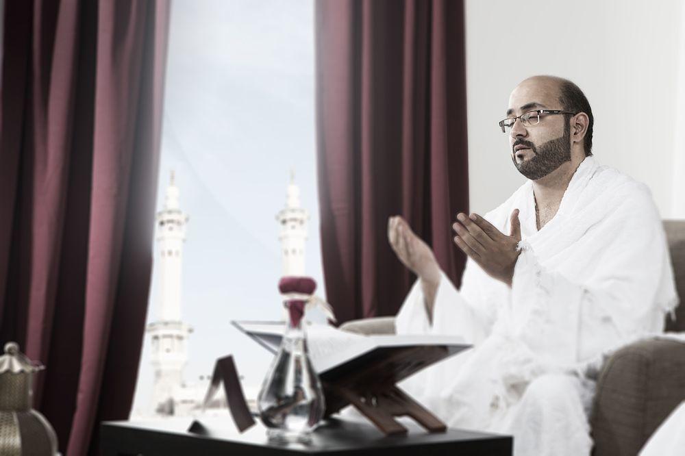 Makarem Ajyad Makkah Hotel Mekka Zewnętrze zdjęcie The photo depicts a man sitting in a room, wearing traditional white garments typically associated with the Hajj pilgrimage. He appears to be engaged in a prayer or spiritual practice, with his hands raised in a gesture of supplication. In the backgr