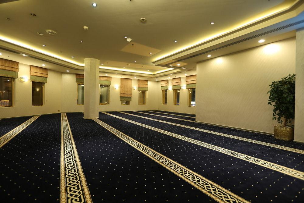 Makarem Ajyad Makkah Hotel Mekka Zewnętrze zdjęcie The photo shows a spacious indoor area with a plush blue carpet featuring a decorative pattern. The room is well-lit, with soft lighting along the ceiling. There are several windows, allowing natural light to enter, and a few plants are positioned ar