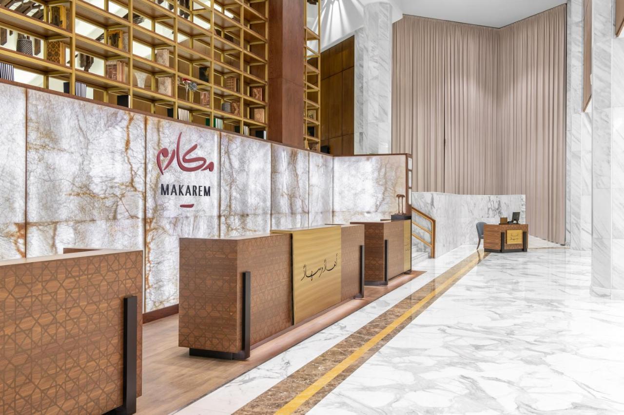 Makarem Ajyad Makkah Hotel Mekka Zewnętrze zdjęcie The photo shows a modern hotel reception area with a sleek design. The reception desk is made of a combination of wood and stone, featuring a warm color palette. The backdrop is adorned with a marble finish, giving a luxurious feel. Above the desk, t