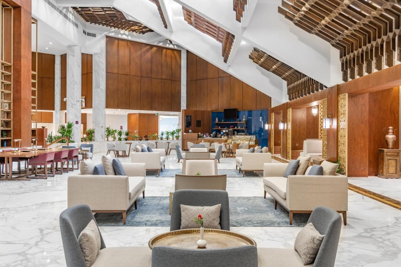 Makarem Ajyad Makkah Hotel Mekka Zewnętrze zdjęcie The photo depicts the interior of a modern and elegantly designed lobby or lounge area. It features a spacious layout with high ceilings, showcasing a combination of wooden elements and marble flooring. 

In the center, there are several seating arra