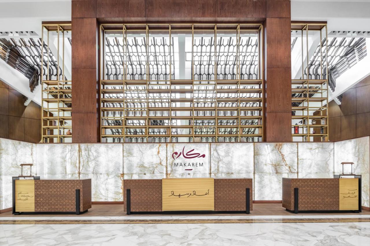 Makarem Ajyad Makkah Hotel Mekka Zewnętrze zdjęcie The photo shows the interior of a hotel or a reception area, characterized by a modern and elegant design. In the foreground, there are multiple reception desks with a polished finish. Behind the desks, a striking feature is a wooden wall with a geom