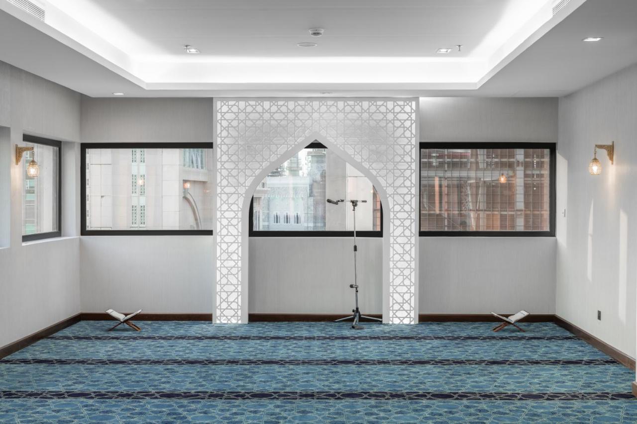Makarem Ajyad Makkah Hotel Mekka Zewnętrze zdjęcie The image shows a prayer room or small mosque interior. It features a white decorative wall with an archway that is typical in Islamic architecture. The floor is covered with a blue carpet, arranged with patterned lines, likely indicating prayer spot