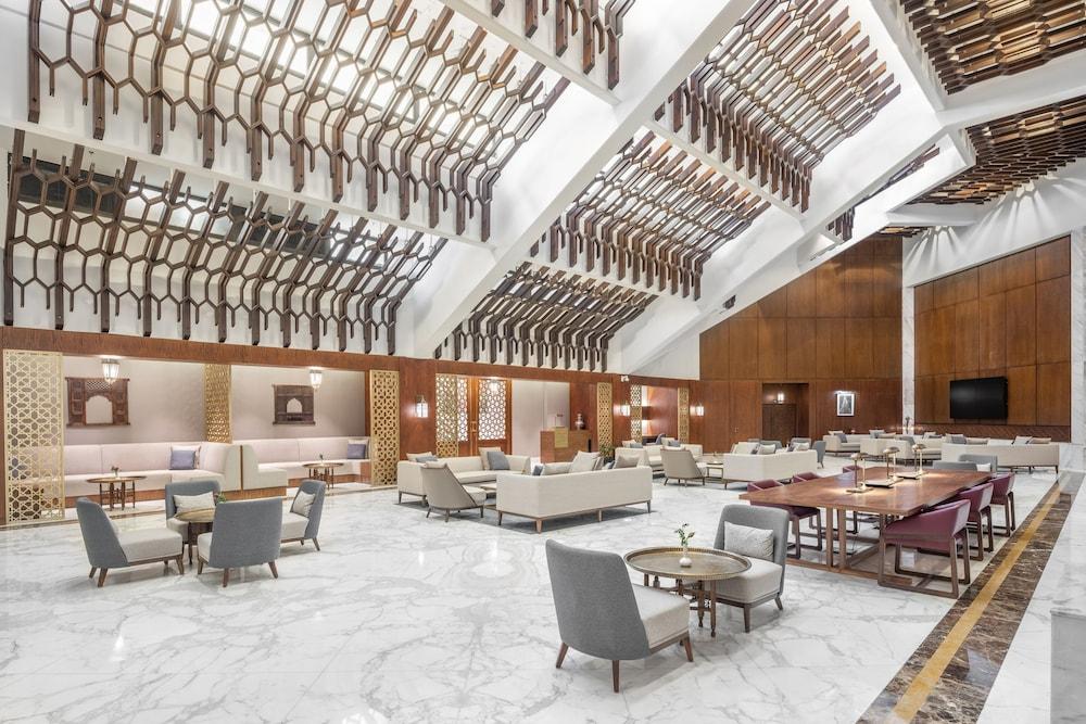 Makarem Ajyad Makkah Hotel Mekka Zewnętrze zdjęcie The photo shows a spacious and elegantly designed lobby area, likely within a hotel. The interior features high ceilings with a unique architectural design, showcasing wooden elements arranged in a geometric pattern. The flooring is a polished marble