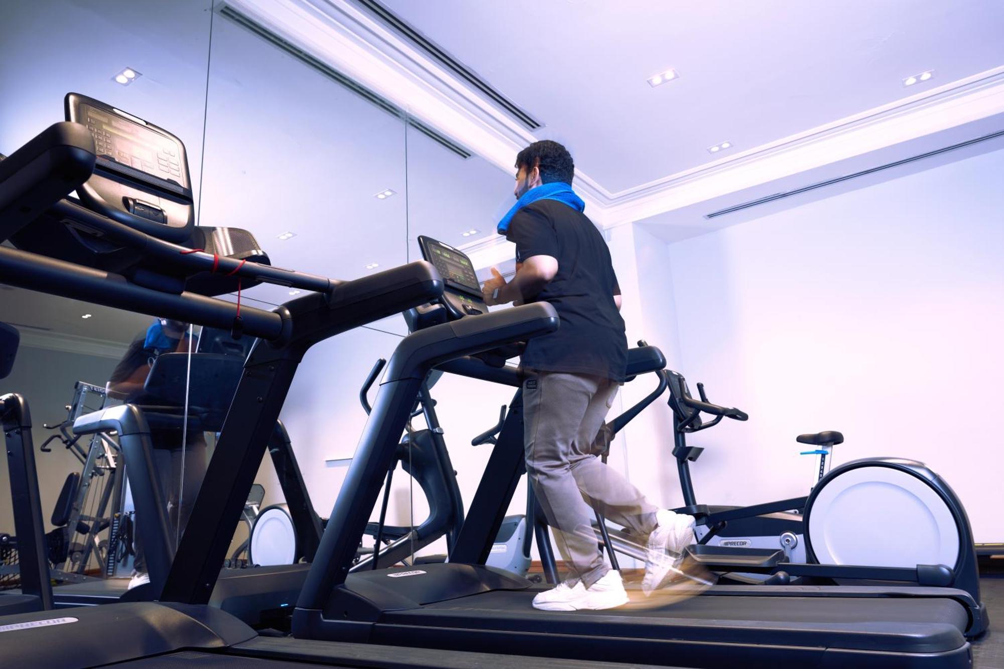 Makarem Ajyad Makkah Hotel Mekka Zewnętrze zdjęcie The photo shows a person exercising on a treadmill in a modern gym or fitness room. The individual is wearing a blue neck support while jogging on the treadmill, which is set against a backdrop of large mirrors. There are also additional exercise equ