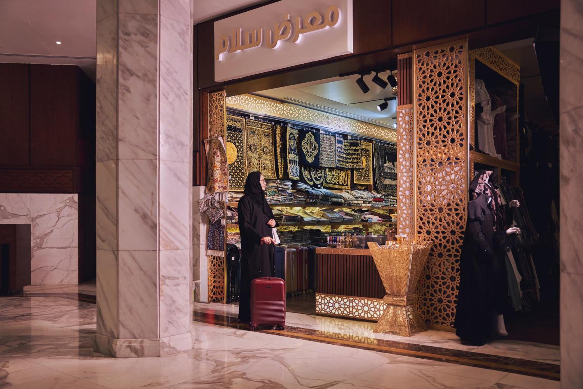 Makarem Ajyad Makkah Hotel Mekka Zewnętrze zdjęcie The photo shows a storefront that appears to sell traditional textiles or garments. The entrance features intricate decorative patterns, typical of Middle Eastern architecture. A woman is standing outside the shop, dressed in a black abaya, and she h