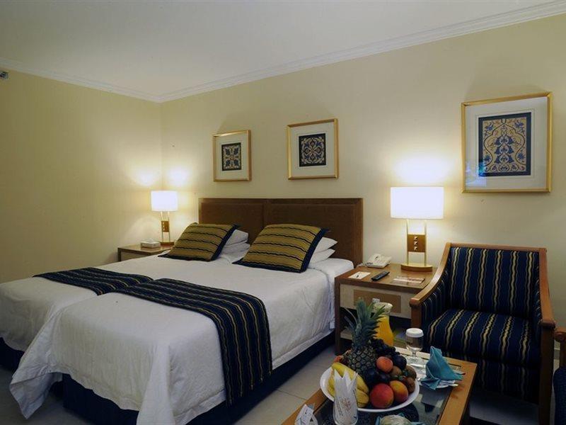 Makarem Ajyad Makkah Hotel Mekka Zewnętrze zdjęcie The photo shows a hotel room with a cozy and inviting atmosphere. It features two beds with white linens and dark striped bedspreads. There are two bedside lamps providing warm light, and the walls are decorated with framed artworks. Beside the beds 