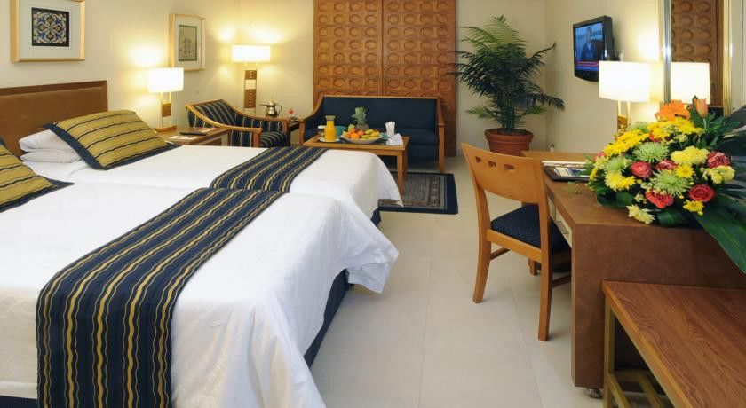 Makarem Ajyad Makkah Hotel Mekka Zewnętrze zdjęcie The image shows a hotel room featuring two beds with white linens and a decorative stripe along the edge. There is a seating area with two chairs and a small table, set with a breakfast spread that includes fruit and drinks. A small potted plant adds