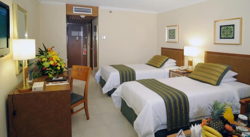 Makarem Ajyad Makkah Hotel Mekka Zewnętrze zdjęcie The photo shows an interior of a hotel room featuring two twin beds with white linens and green decorative accents. The walls are painted in a light beige color, and there is a small table next to one of the beds. A desk with a chair is positioned ne