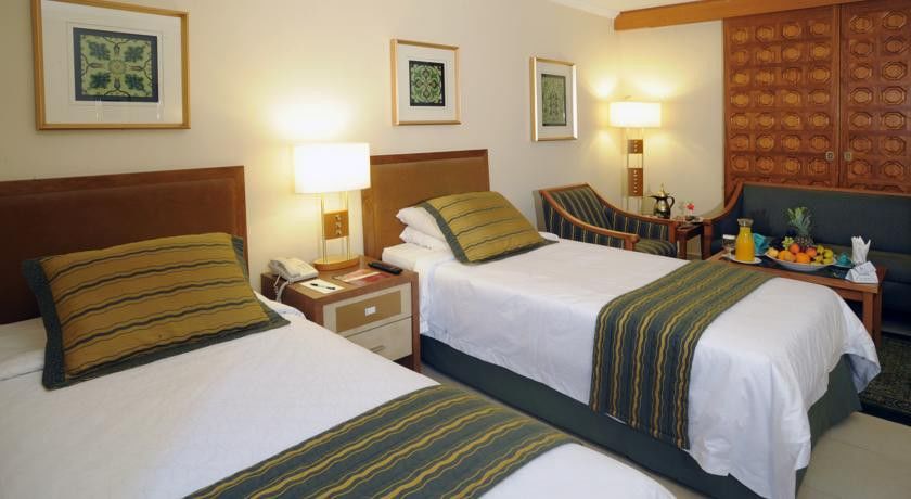 Makarem Ajyad Makkah Hotel Mekka Zewnętrze zdjęcie The photo shows a hotel room with two twin beds, each topped with decorative green and gold striped bed runners. There is a nightstand between the beds with a lamp on it. The room features light-colored walls, framed artwork on the walls, and a small