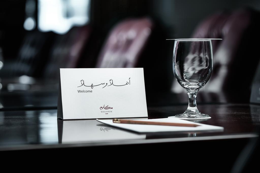 Makarem Ajyad Makkah Hotel Mekka Zewnętrze zdjęcie The photo depicts a well-arranged table setting. There is a card in both Arabic and English that says "Welcome," placed on the table. Next to the card, there is a clear glass and a pen resting on a piece of paper. The background features leather seat