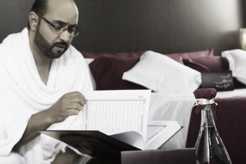 Makarem Ajyad Makkah Hotel Mekka Zewnętrze zdjęcie The photo shows a man engaged in reading a book or document, seated in a room with a relaxed atmosphere. He is wearing traditional white attire, often associated with specific cultural or religious practices. In the foreground, there is a bottle, pos